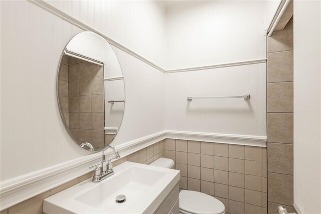 bathroom featuring toilet, tile walls, and sink