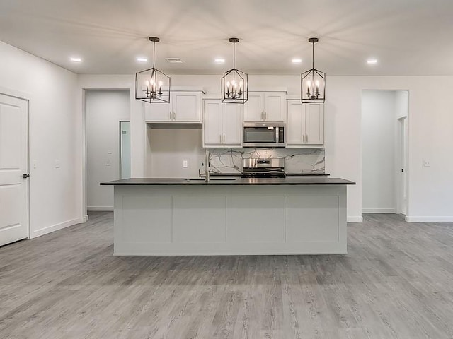 kitchen with white cabinets, hanging light fixtures, stainless steel appliances, and a kitchen island with sink