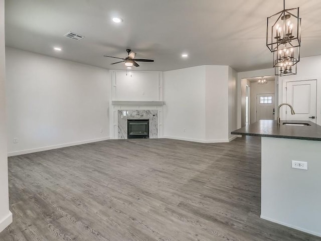 unfurnished living room featuring dark hardwood / wood-style flooring, sink, a fireplace, and ceiling fan with notable chandelier