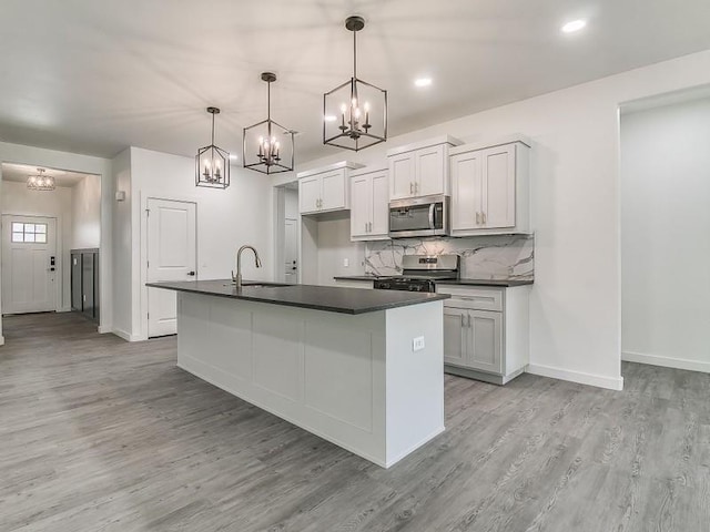 kitchen with pendant lighting, white cabinets, stainless steel appliances, and a center island with sink