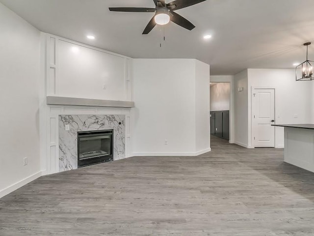 unfurnished living room with a high end fireplace, ceiling fan with notable chandelier, and light hardwood / wood-style flooring