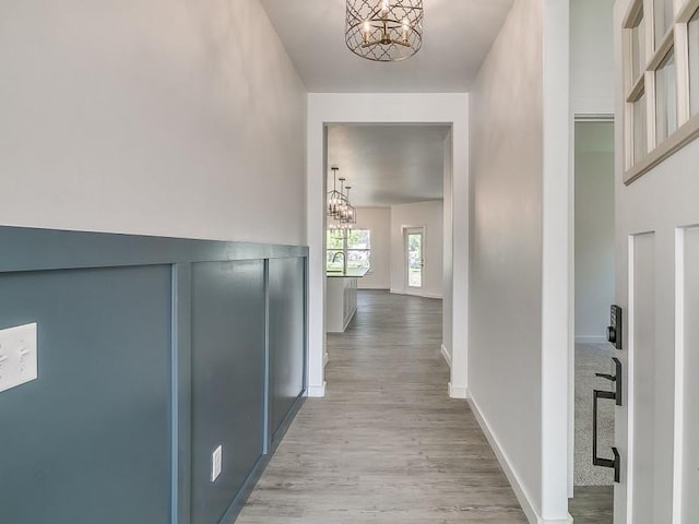 corridor with light hardwood / wood-style floors and an inviting chandelier