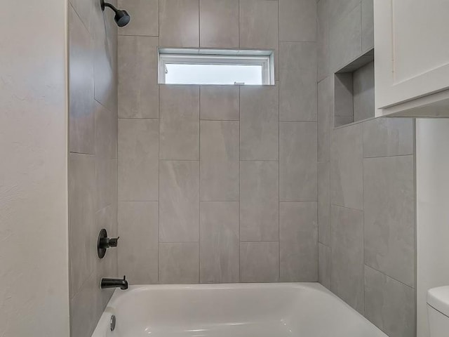 bathroom featuring tiled shower / bath combo and toilet