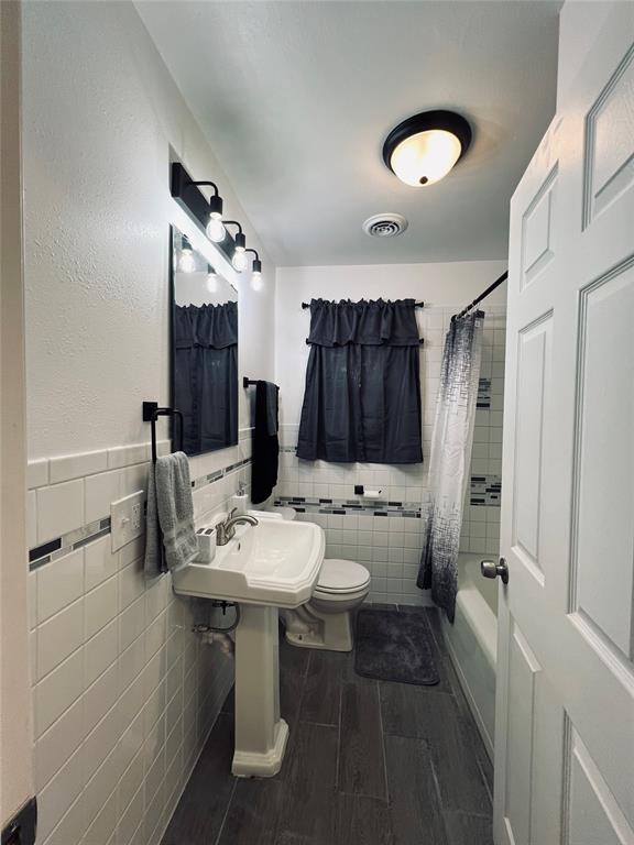 full bathroom featuring shower / bath combination with curtain, toilet, tile walls, and sink