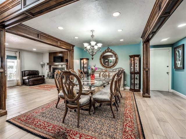 dining area with a textured ceiling, light wood-type flooring, and an inviting chandelier