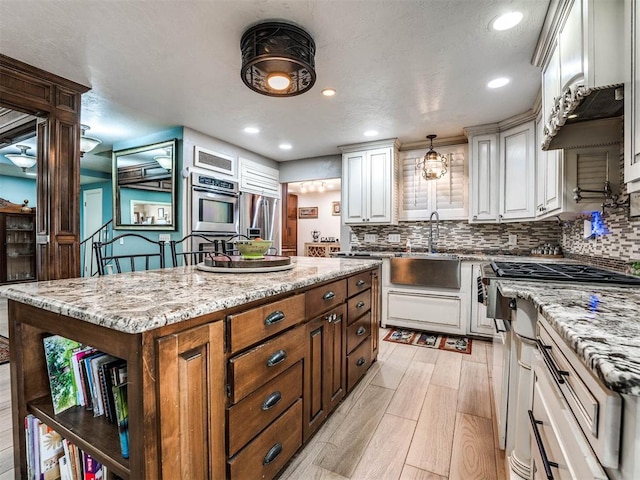 kitchen with white cabinetry, sink, light stone countertops, a kitchen island, and appliances with stainless steel finishes