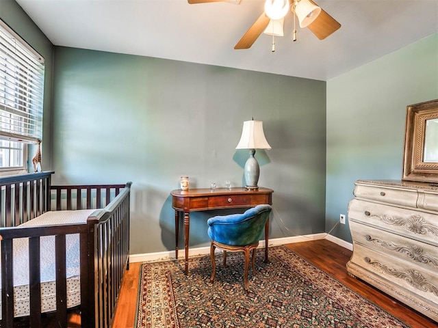 bedroom featuring hardwood / wood-style floors, a nursery area, and ceiling fan