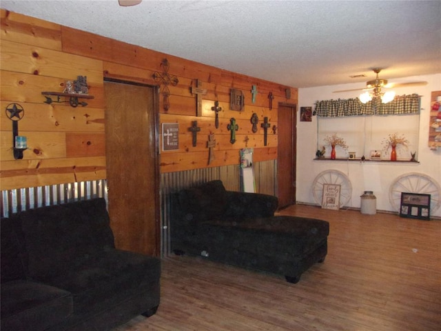 living room featuring wood walls, ceiling fan, wood-type flooring, and a textured ceiling