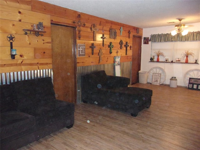 living room featuring wood-type flooring, ceiling fan, and wooden walls