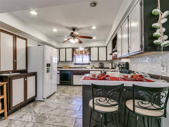 kitchen featuring ceiling fan, white fridge with ice dispenser, sink, kitchen peninsula, and a breakfast bar area