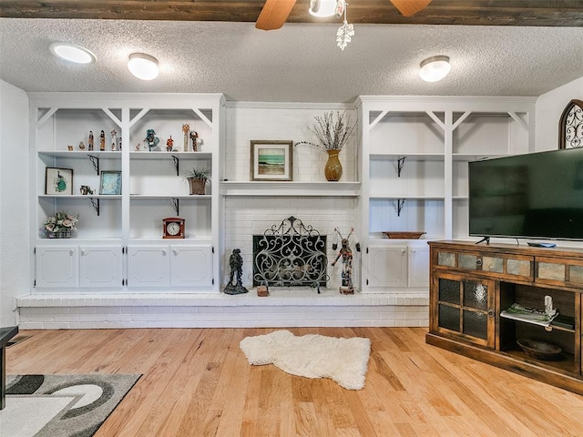 living room with ceiling fan, a fireplace, a textured ceiling, and light wood-type flooring