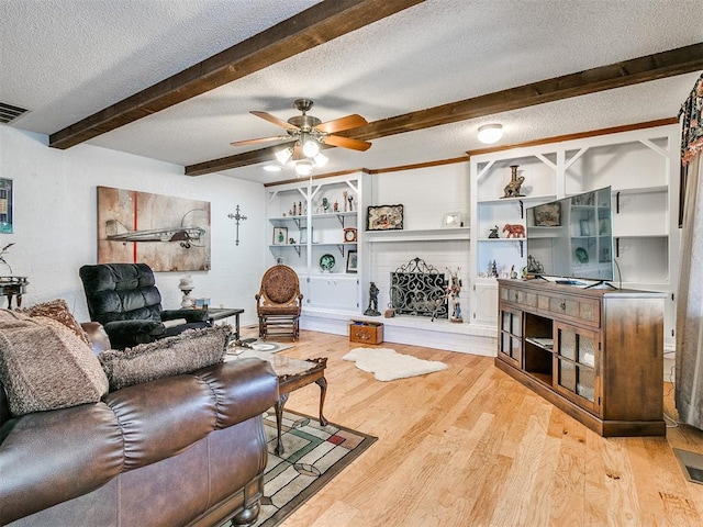 living room with beam ceiling, ceiling fan, light hardwood / wood-style flooring, a textured ceiling, and a fireplace