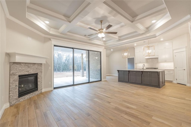 unfurnished living room featuring ornamental molding, a stone fireplace, light wood finished floors, and coffered ceiling