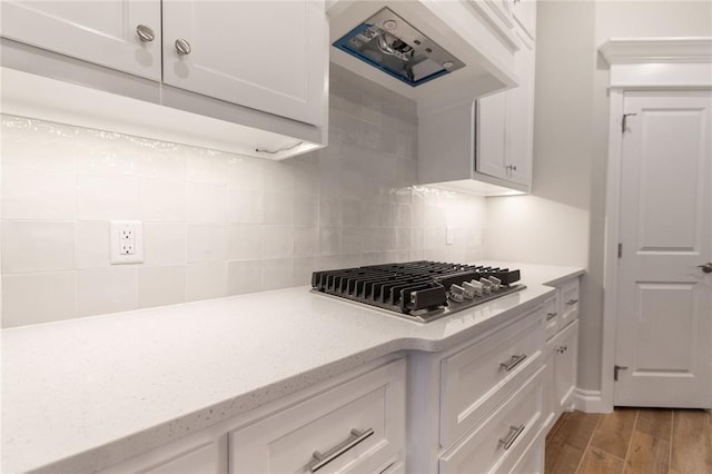 kitchen with stainless steel gas cooktop, extractor fan, light wood-style floors, white cabinetry, and backsplash