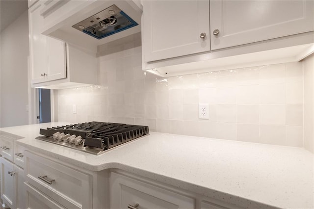 kitchen with light stone countertops, white cabinets, backsplash, range hood, and stainless steel gas stovetop