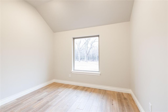 empty room featuring lofted ceiling, light wood-type flooring, and baseboards