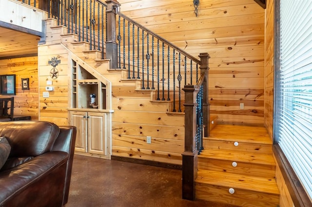 staircase featuring concrete floors, wooden ceiling, and wooden walls