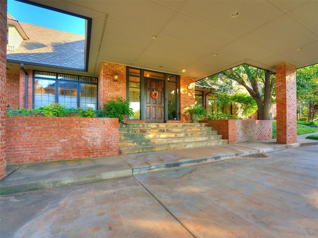 entrance to property featuring a shingled roof and brick siding