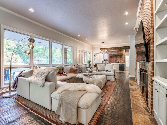 living room featuring a brick fireplace, wood-type flooring, a chandelier, a textured ceiling, and ornamental molding