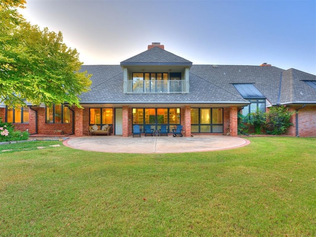 back house at dusk featuring a lawn, a balcony, and a patio