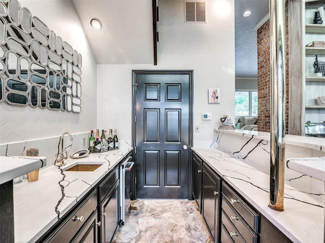 kitchen with light stone countertops, vaulted ceiling, and sink