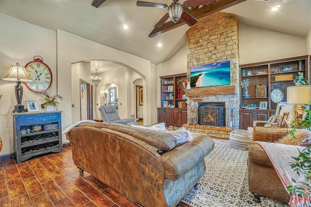 living room with dark wood-type flooring, high vaulted ceiling, ceiling fan with notable chandelier, a stone fireplace, and beamed ceiling