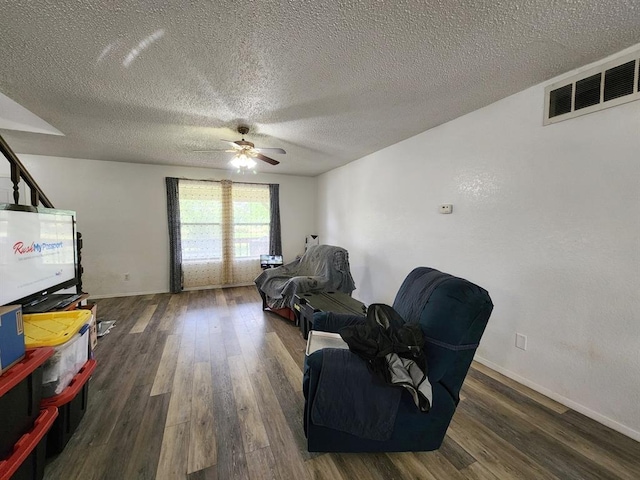 living area with ceiling fan, dark hardwood / wood-style flooring, and a textured ceiling