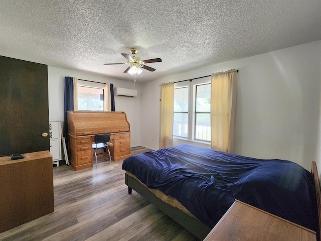 bedroom featuring hardwood / wood-style floors, ceiling fan, an AC wall unit, and a textured ceiling