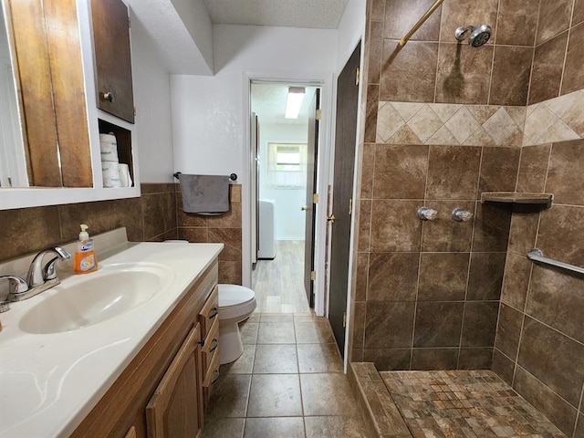 bathroom featuring vanity, toilet, a textured ceiling, tile walls, and a tile shower