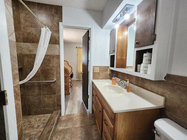 bathroom featuring a shower with curtain, vanity, a textured ceiling, tile walls, and toilet