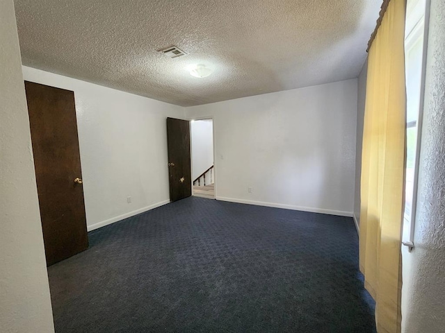 spare room with a textured ceiling and dark colored carpet