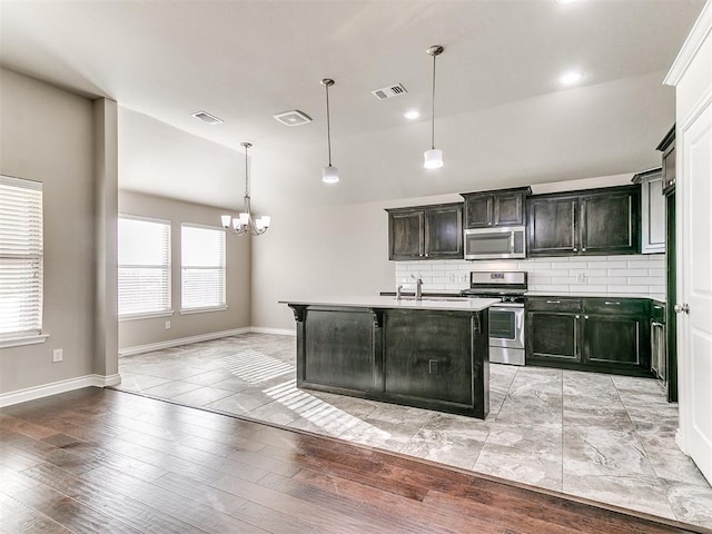 kitchen featuring pendant lighting, light wood-type flooring, stainless steel appliances, and a kitchen island with sink