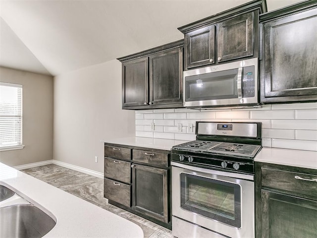 kitchen featuring backsplash, dark brown cabinets, stainless steel appliances, vaulted ceiling, and sink