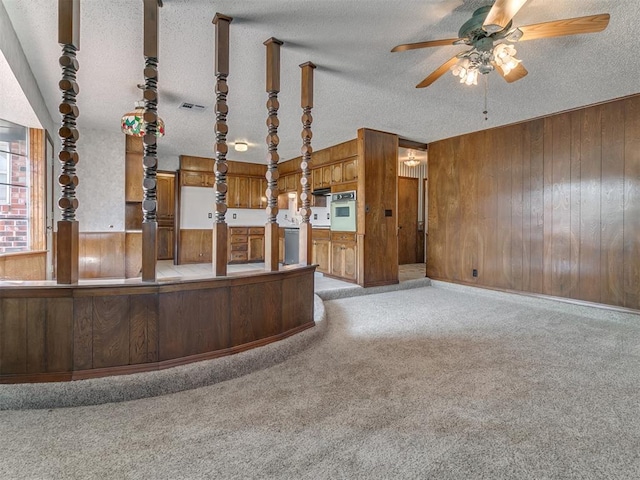 interior space featuring a textured ceiling, hanging light fixtures, wooden walls, and light carpet