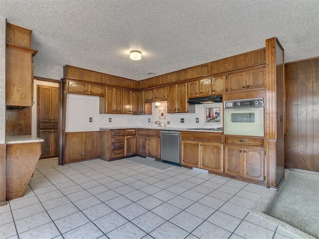 kitchen featuring a textured ceiling, white appliances, light tile patterned floors, and wood walls