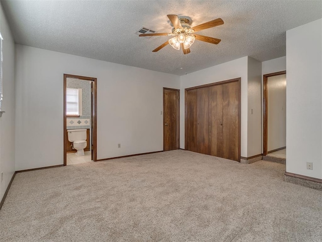 unfurnished bedroom with ensuite bathroom, ceiling fan, a textured ceiling, light colored carpet, and a closet