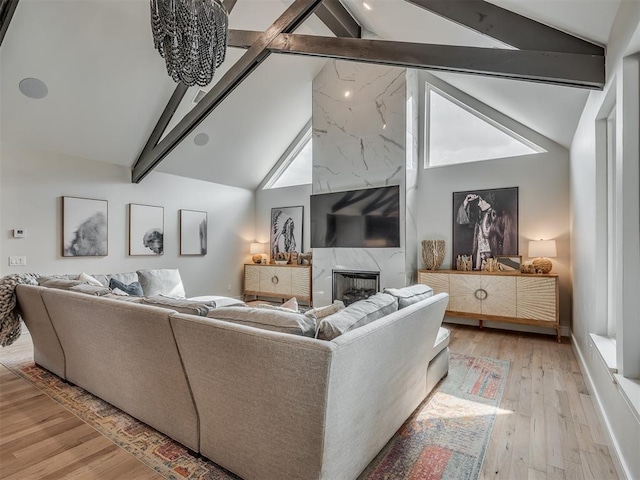 living room with beamed ceiling, a chandelier, a high end fireplace, and light hardwood / wood-style flooring