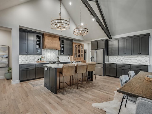 kitchen featuring an inviting chandelier, high end refrigerator, high vaulted ceiling, an island with sink, and pendant lighting