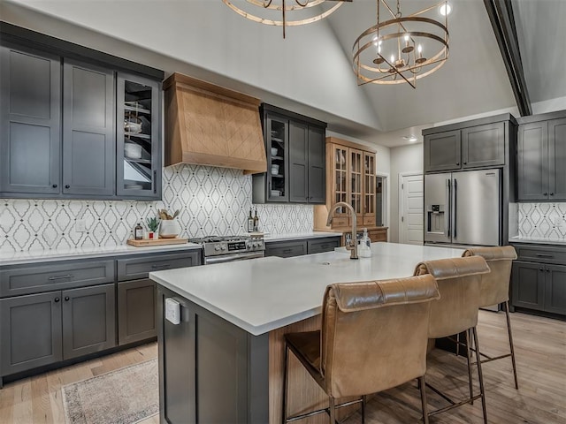 kitchen featuring pendant lighting, premium range hood, a kitchen island with sink, stainless steel appliances, and a chandelier