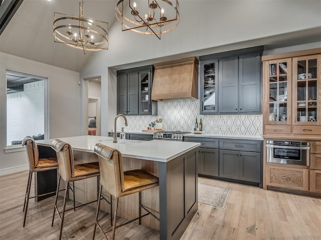 kitchen with premium range hood, stainless steel appliances, an inviting chandelier, hanging light fixtures, and an island with sink