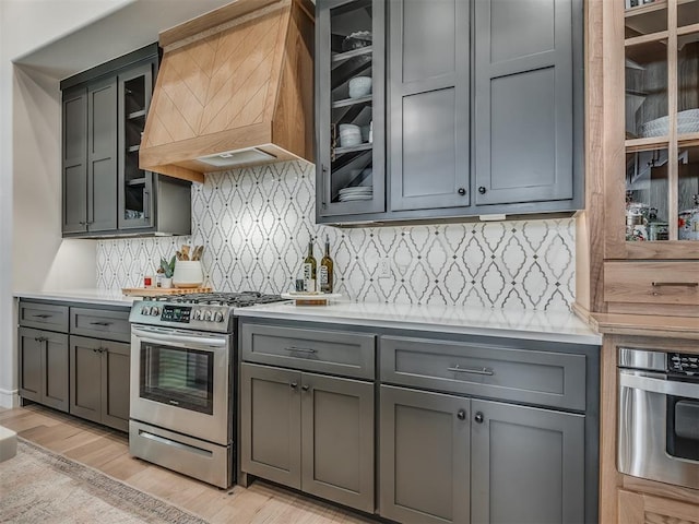 kitchen with backsplash, premium range hood, gray cabinetry, stainless steel appliances, and light hardwood / wood-style floors