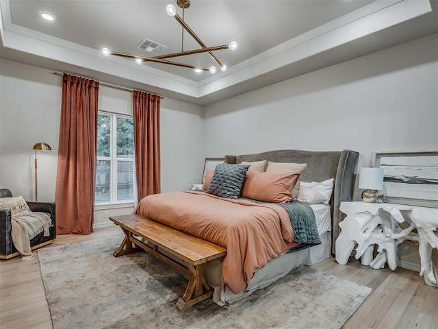 bedroom featuring light wood-type flooring, an inviting chandelier, and a raised ceiling