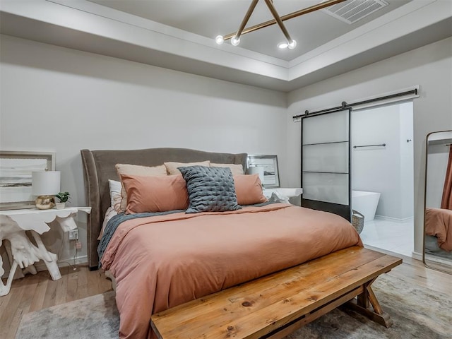 bedroom with hardwood / wood-style floors, a barn door, and a tray ceiling