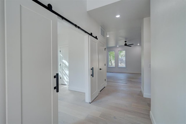 corridor with light wood-type flooring, visible vents, baseboards, and a barn door