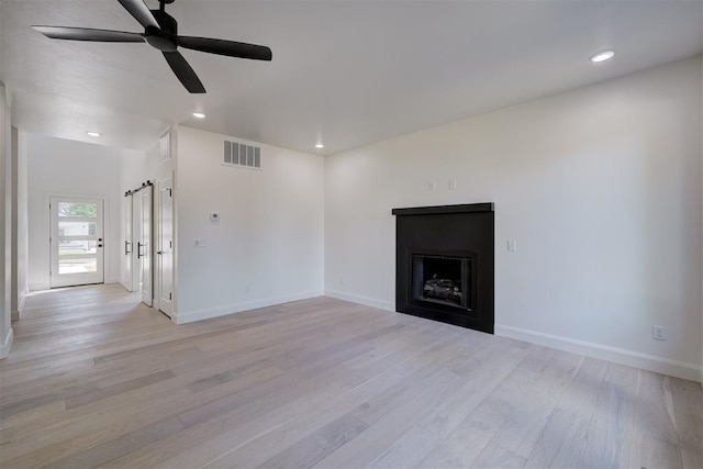 unfurnished living room with ceiling fan, a fireplace, visible vents, and light wood-style floors