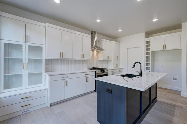 kitchen with wall chimney exhaust hood, a sink, a center island with sink, and white cabinetry