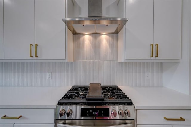 kitchen featuring wall chimney range hood, stainless steel gas range, white cabinetry, and light countertops