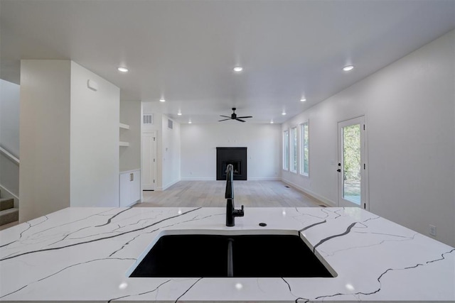 kitchen featuring light stone counters, open floor plan, a fireplace, a sink, and recessed lighting