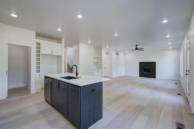 kitchen featuring a fireplace, a center island with sink, stainless steel dishwasher, white cabinetry, and a sink