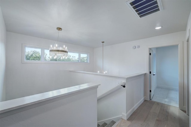 hallway with light wood-style flooring, visible vents, a chandelier, and an upstairs landing